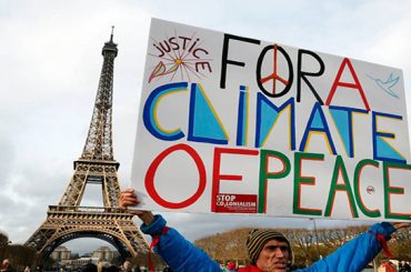 Jean-Baptiste Redde aka Voltuan holds a banner reading "For a climate of peace" during a rally held by several Non Governmental Organisations (NGO) to form a human chain on the Champs de Mars near the Eiffel Tower in Paris on December 12, 2015 on the sidelines of the COP21, the UN conference on global warming.
French hosts submit the final version of a global climate-saving pact to negotiators at UN Conference on december 12. The goal is for ministers to approve the agreement by the end of the day but that could be extended one more day. / AFP / FRANCOIS GUILLOT        (Photo credit should read FRANCOIS GUILLOT/AFP/Getty Images)
